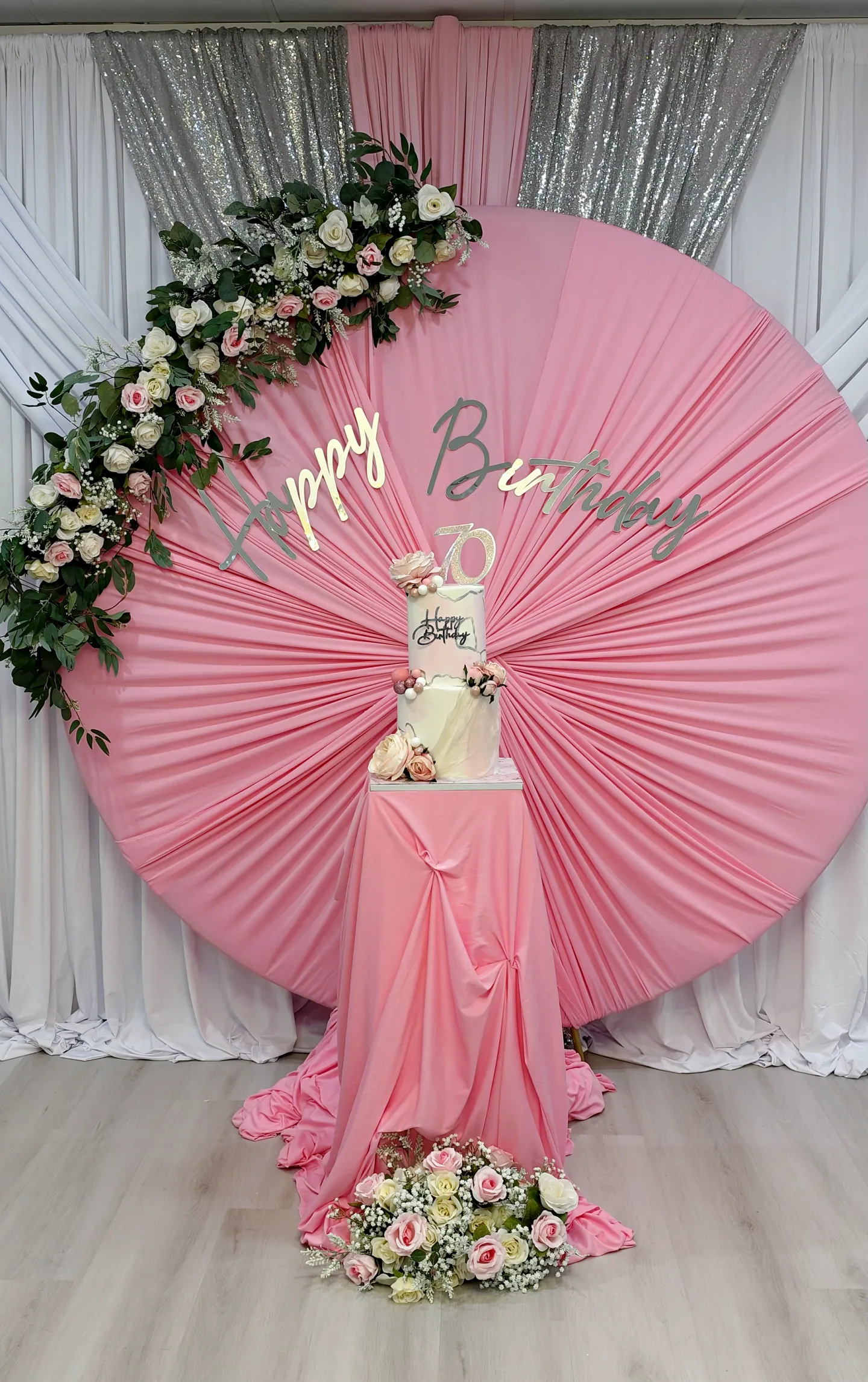 A pink circular birthday backdrop with flowers and a cake in The Victoria.