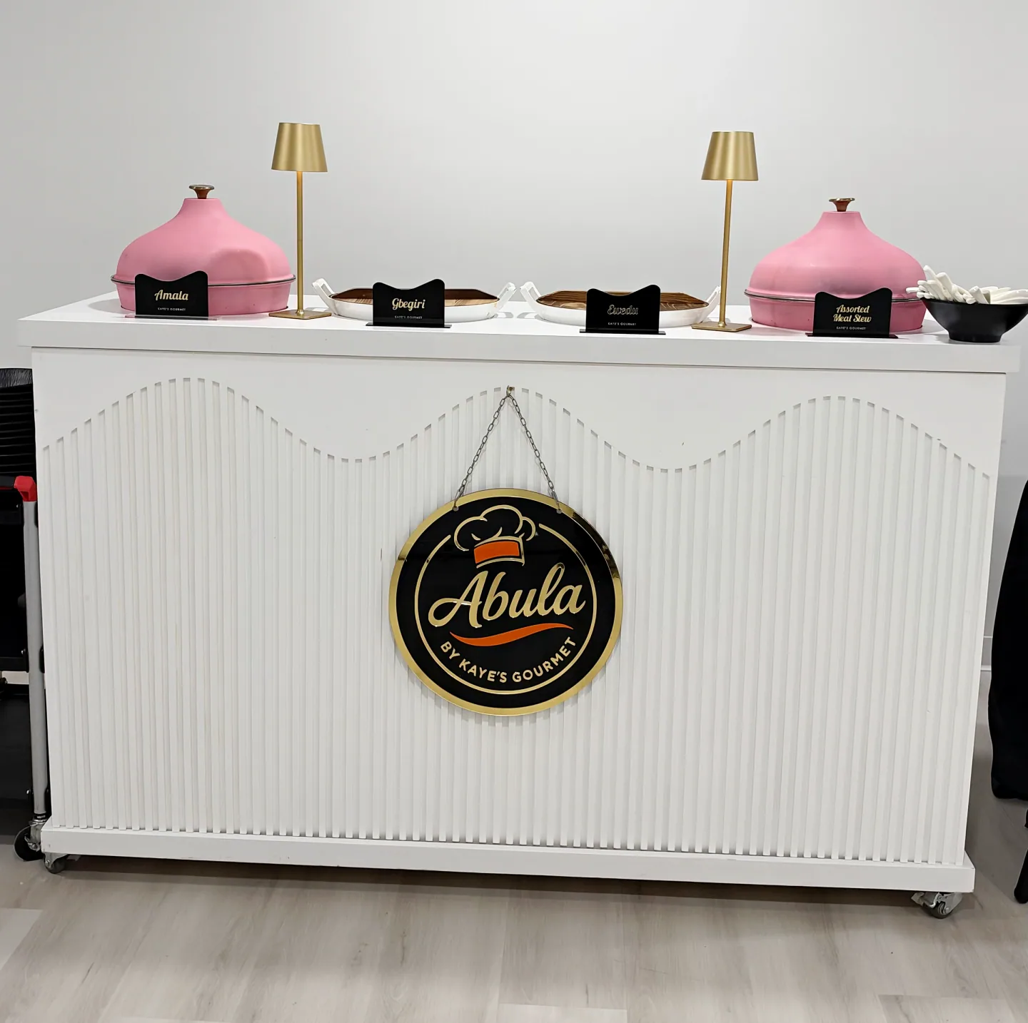 A white Abula service counter with pink serving pots and gold lamps.